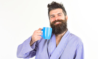 Man with beard and mustache holds mug of coffee, isolated on white. Morning coffee concept. Macho in bathrobe drinks tea or coffee with smiling face.