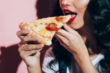 partial view of woman eating pizza on pink background