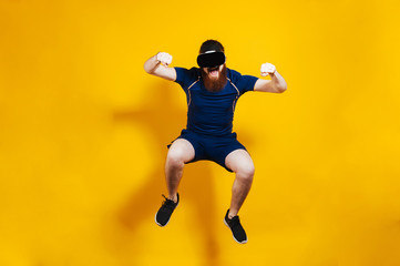 Fototapeta na wymiar Sportsman in sportwear jumping over yellow background and wearing VR goggles. Man in virtual reality