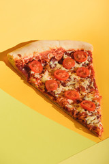 close up view of piece of italian pizza with cherry tomatoes on colorful backdrop