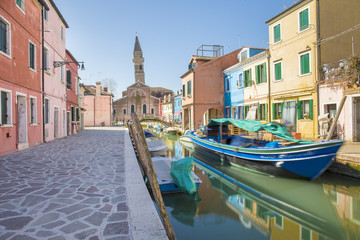Fototapeta na wymiar Typical canal with colorful facades with vibrant colors and Church of San Martino and its leaning campanile in famous fishermen village on the island of Burano, Venice, Italy