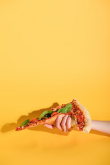 partial view of woman holding piece of pizza in hand on yellow background