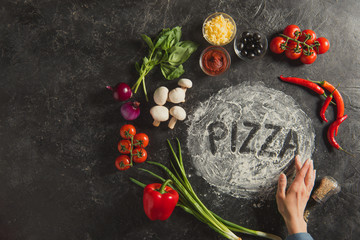 Obraz na płótnie Canvas partial view of female hand, fresh ingredients and pizza lettering made of flour on dark surface