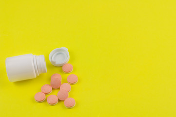 Heap of double color whole pills beside plastic container and cap on background of yellow paper