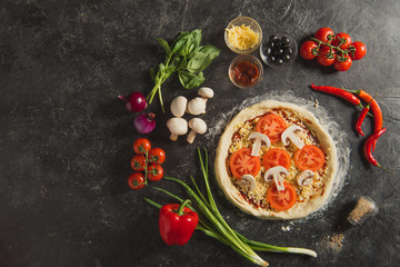 top view of raw italian pizza and fresh ingredients around on dark surface