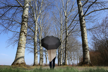 Frau steht mit Sonnenschirm auf einem Waldweg