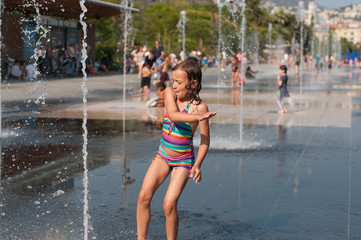 Little girl plays in fontaine at July summer heat