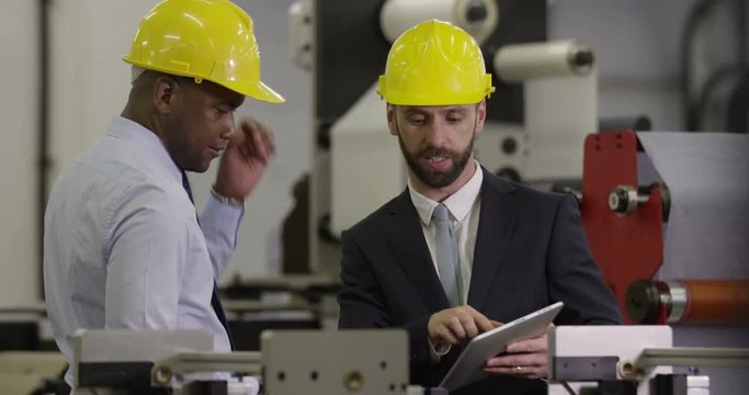 Manager discusses work with a factory worker on a digital tablet.