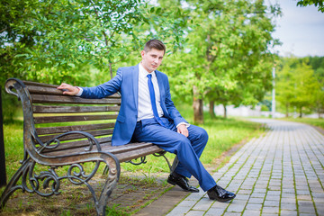 Stylish groom in blue suit, sitting on bench in park