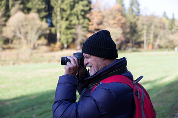 Senior man taking a photo with camera in the woods
