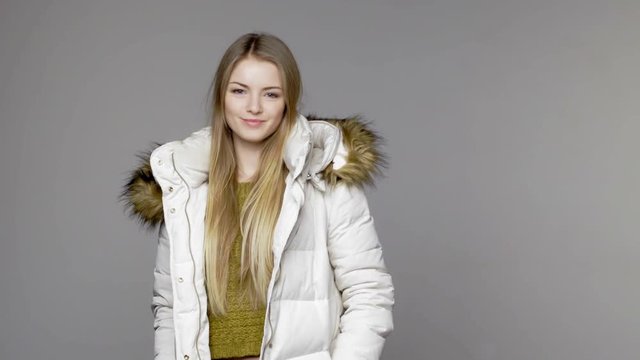 Blond woman wearing warm winter coat with fur hood smiling at camera