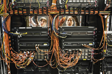 Caucasian female and Asian American male technicians working on a CAT 5 cable bundling system in a large computer server room.