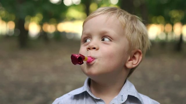 Happy little boy are blowing into unfolding tube at a birthday party. Little boy having fun and blows a party horn. Little boy with birthday pipes.