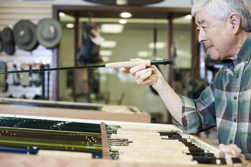 Asian American senior male checking the balance on a 5 weight fly fishing rod for sale in a fly-fishing shop.