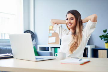 Job well done. Young woman relaxing in front of laptop in home office