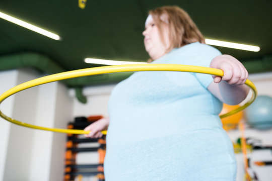 Portrait of young obese woman working out with hula hoop in fitness club, focus on foreground - Powered by Adobe
