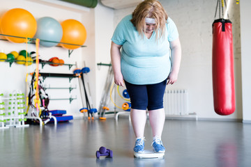 Full length portrait of big overweight woman standing on scales after fitness training, copy space
