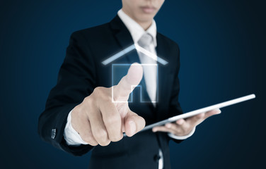 Businessman holding digital tablet and touching house icon on screen, on blue background