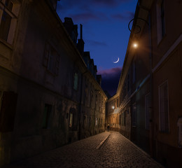 Narrow ancient street of the old city and the moon in the clouds in the sky. night photo. Brasov. Romania. Europe.
