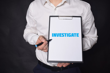 In the hands of a businessman a notebook with the inscription:INVESTIGATE