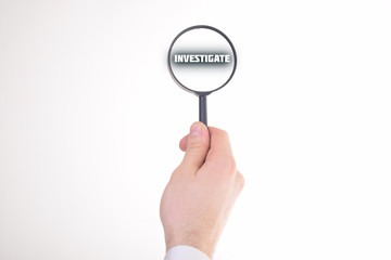 Businessman looking at a magnifying glass word:INVESTIGATE