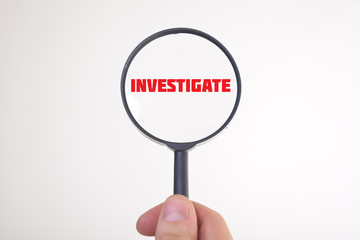 Businessman looking at a magnifying glass word:INVESTIGATE