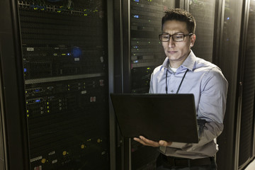 Hispanic man technician doing diagnostic tests on computer servers in a large server farm.