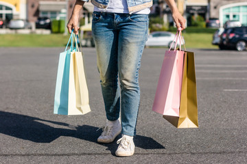 Close up of a young Asian woman shopping an outdoor flea market with a background of pastel bulidings and blue sky. Young woman smile with a colorful bag in her hand. Outdoor shopping concept.