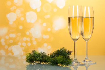 Glasses with champagne, new year's pine branch on yellow background