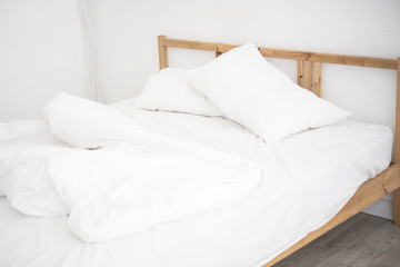 white bedding sheets and pillow in white bedroom. Messy and crumpled bed concept.