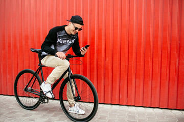 Cheerful guy sitting on bike and using a smartphone