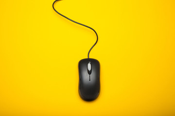 Black computer mouse on a yellow background.