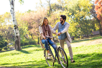 Happy young couple having fun riding a bicycle on sunny day in the park.	