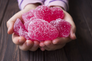 baby hands holding pink marmalade on wooden background