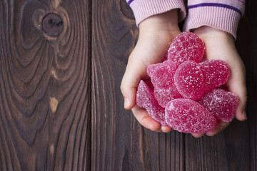 baby hands holding pink marmalade on wooden background