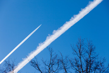 Condensation trace highlighted by the setting sun behind a twin-engine turbojet passenger plane in the March sky. There is a scattered track from the recently flown another liner