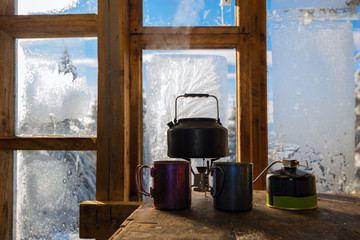 Small kettle stands on a gas burner next to steel cups