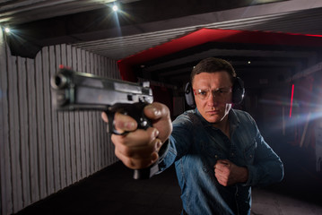 An adult man in jeans trains to shoot a gun in a closed dash.