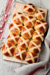 Easter traditional hot cross buns homemade on wooden tray with linen textile and willow branches on white wooden background. Selective focus. Top view. Copy space.