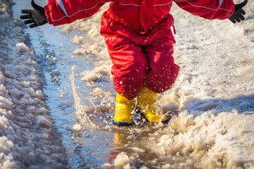 Kid in rainboots jumping in the ice puddle