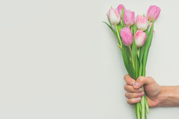 Man's hand holding bouquet of first spring pink tulips on white background with copy space. Beautiful spring background for International Womens day, Mother's day, March 8, Valentines day