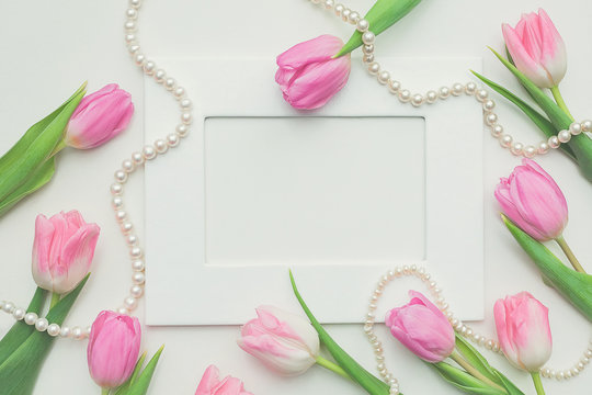 Top view of pink tulips, photo frame and string of pearls on white background with copy space. Beautiful spring background for International Womens day, Mother's day, March 8, Valentines day