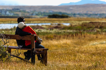 Couple in love, smiling towards horizon, in wooden bench in natu
