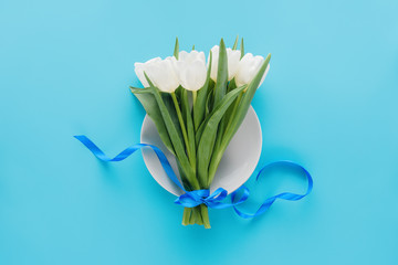 Top view of white tulips on plate isolated on blue