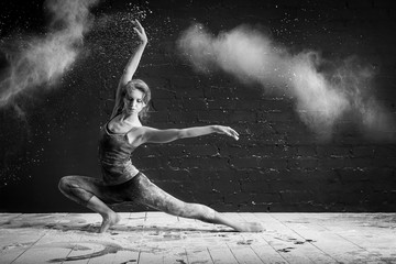 beautiful ballet dancer dancing barefoot on black background in a cloud of dust