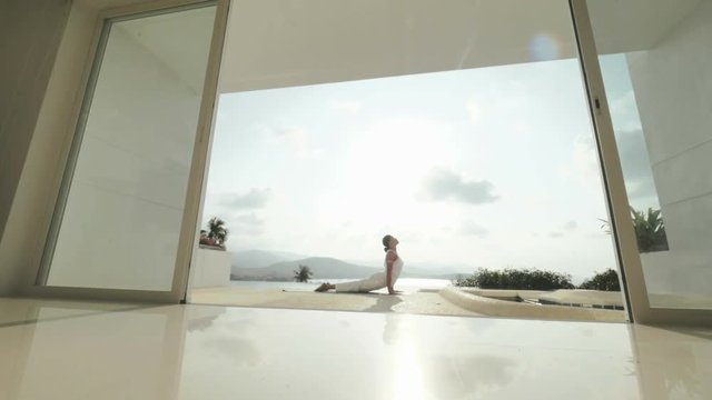 Woman practicing yoga exercises on outdoor terrace with sea and hill landscape