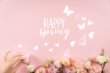 Top view of hand arranging beautiful tender flowers with HAPPY SPRING sign and butterflies isolated on pink background