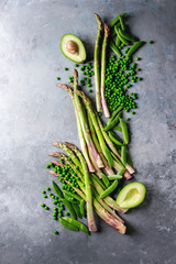 Variety of raw uncooked organic young green vegetables asparagus, peas, pod pea, avocado over grey texture background. Top view, copy space. Healthy eating