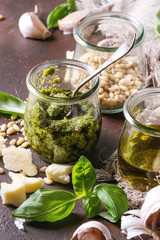 Traditional Basil pesto sauce in glass jar with ingredients above fresh basil, olive oil, parmesan cheese, garlic, pine nuts, lemon on cloth over dark texture background. Close up