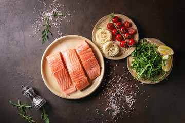 Sliced raw uncooked salmon fillet on ceramic plate with ingredients for dinner, arugula, lemon,...
